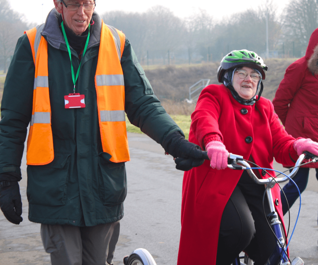 Photo of a man guiding a lady with special needs on a trike around the Moredon track