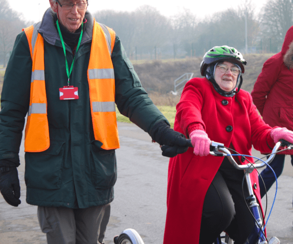 Photo of a man guiding a lady with special needs on a trike around the Moredon track