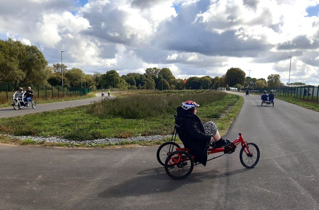 Photograph taken at the Moredon Sporting Hub cycling track showing people trying out adapted cycles in the "Limitless" sessions.