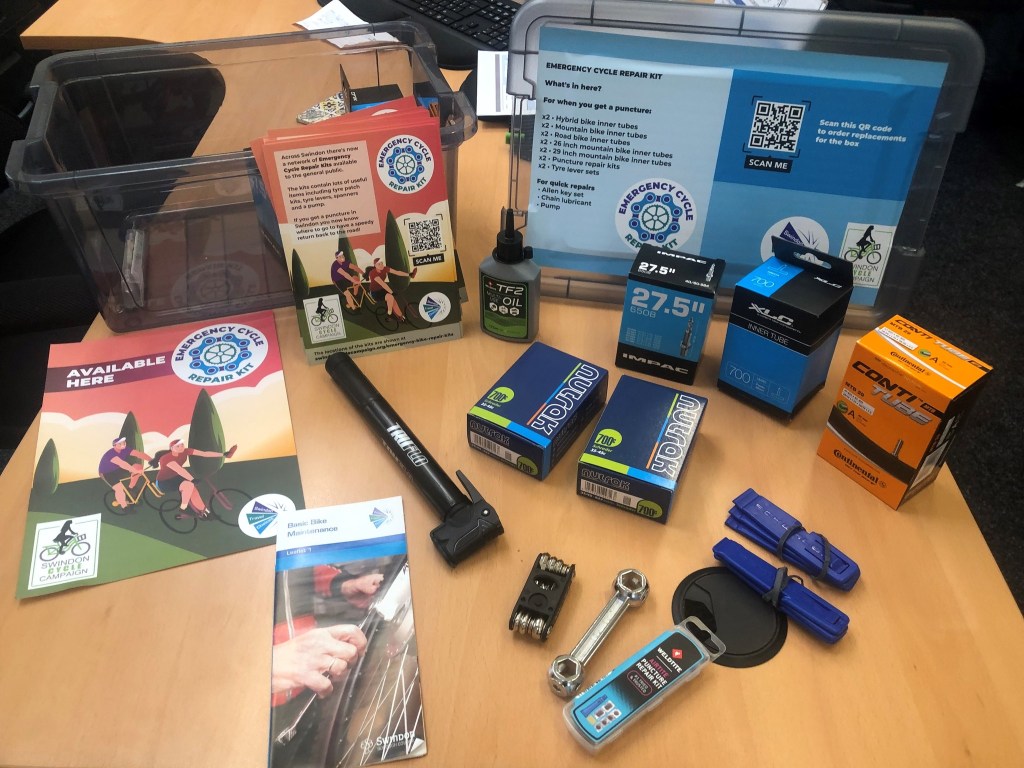 Photograph showing a bike kit with the contents laid out on the table; inner tubes, spanners, pump, oil and tools