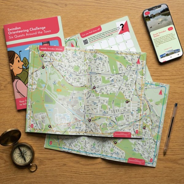 Photo of the new orienteering map booklet open at a page with a phone and a compass next to it.