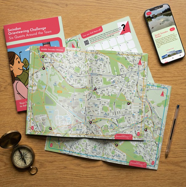 Photo of the new orienteering map booklet open at a page with a phone and a compass next to it.