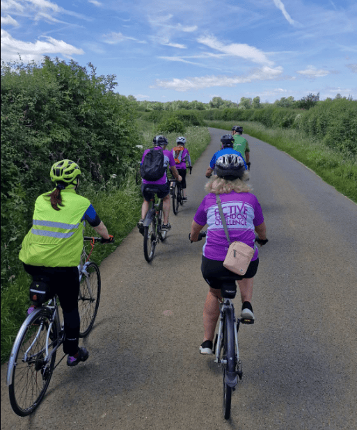 Photo of a group of cyclists going down a quiet country road. The picture is shot from the back of the group.